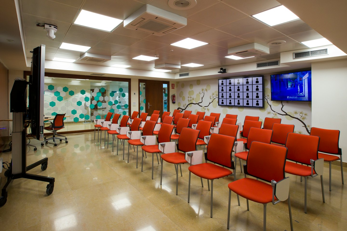 Nowoczesna sala konferencyjna z pomarańczowymi krzesłami i dużymi ekranami.